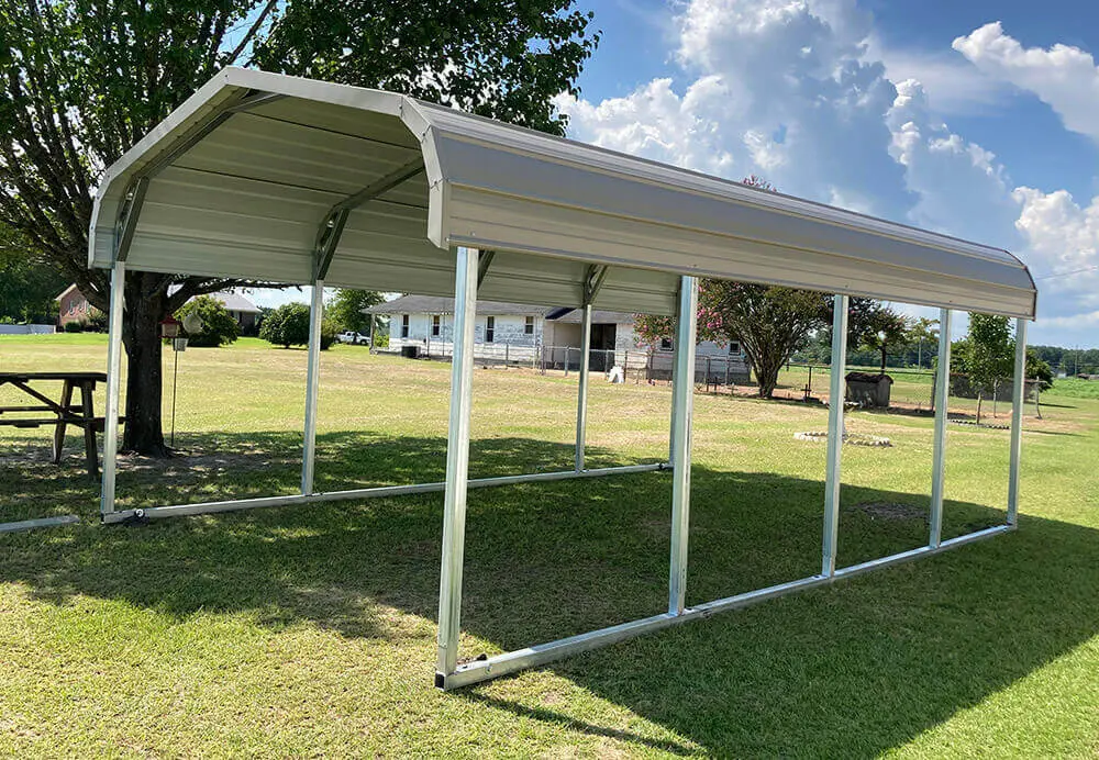 A simple white metal canopy shelter stands on a grassy area under a partly cloudy sky.